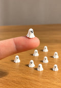 Tiny white 3D printed Halloween ghosts, one balanced on a fingertip